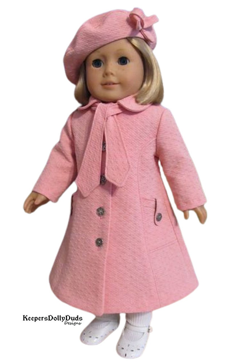 Puede incluir: Un abrigo rosa para mu&ntilde;eca con un gorro a juego y un lazo. El abrigo tiene una corbata en el cuello y botones en la parte delantera. La mu&ntilde;eca lleva zapatos blancos.