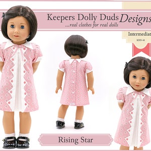 May include: A pink and white dress with a diamond pattern and white trim. The dress has a white collar and a bow at the neck. The dress is for a doll and is labelled "Keepers Dolly Duds Designs" and "Rising Star".