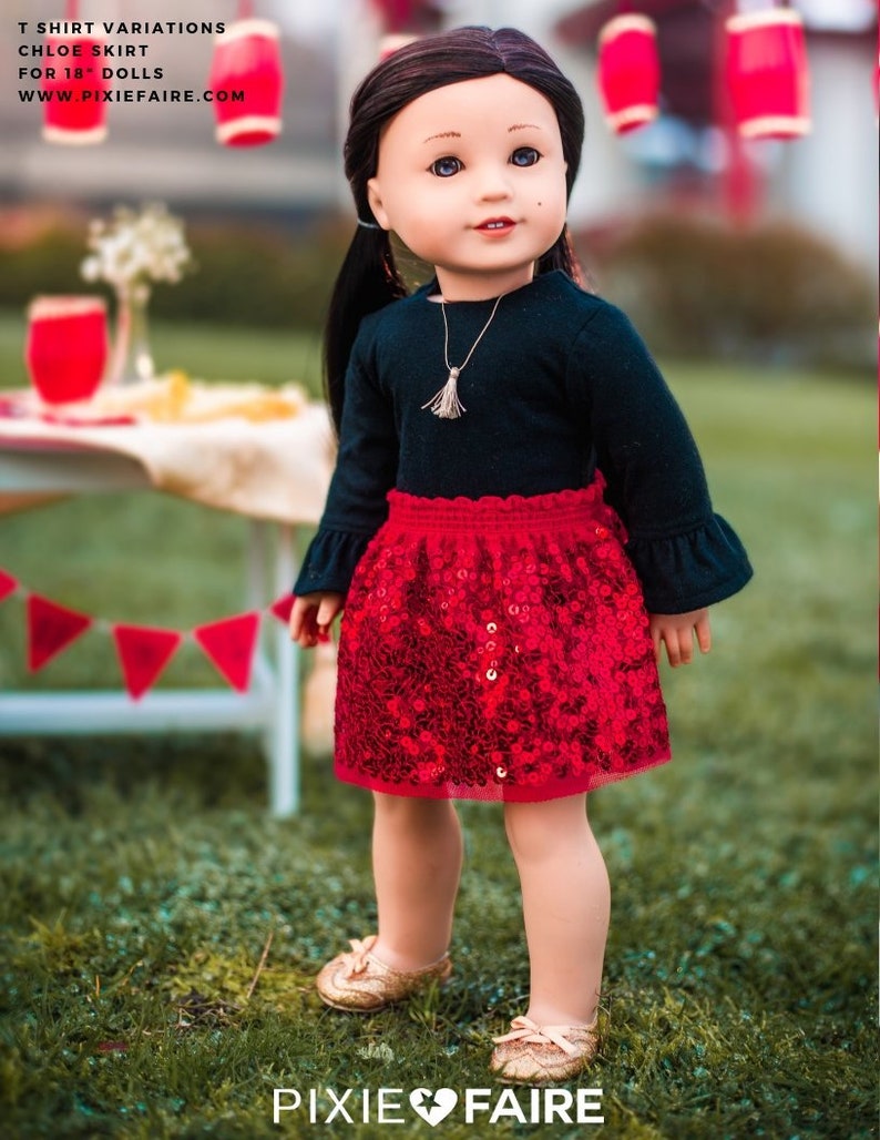 Pu&ograve; includere: Una bambola che indossa una camicia nera a maniche lunghe con una gonna rossa di paillettes. La bambola ha i capelli castani e gli occhi azzurri. La bambola &egrave; in piedi sull'erba verde con decorazioni rosse e bianche sullo sfondo.