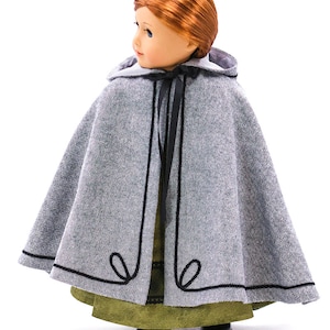 May include: A gray hooded cape with black trim and a black ribbon tie. The cape is made for a doll and is shown on a doll wearing a green dress.