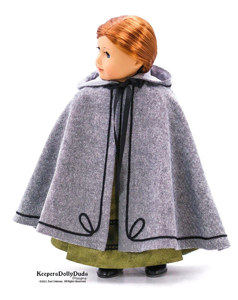 May include: A gray hooded cape with black trim and a black ribbon tie. The cape is made for a doll and is shown on a doll wearing a green dress.
