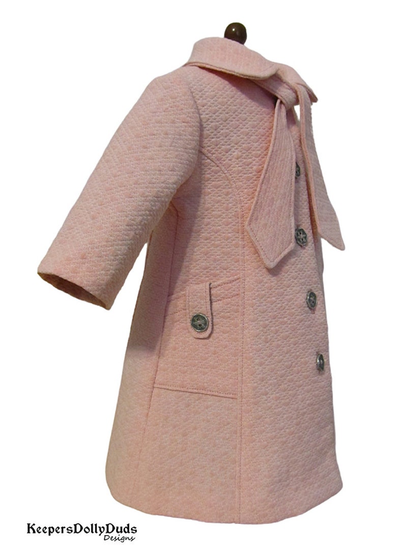 Puede incluir: Un abrigo acolchado rosa con un gran lazo de corbata y botones plateados. El abrigo tiene un bolsillo en el lado izquierdo.