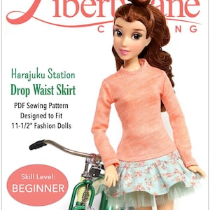 Puede incluir: Una muñeca con una camiseta de manga larga color melocotón y una falda de cintura baja con estampado floral y ribete de tul. La muñeca está junto a una bicicleta verde. El texto dice "Harajuku Station Drop Waist Skirt" y "Designed to Fit 29.2 cm Fashion Dolls."