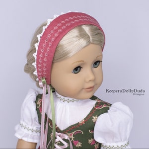 May include: A doll wearing a white blouse with green and gold embroidery, a pink and green ribbon, and a pink headband with white lace trim. The headband has a white embroidered design. The doll has blonde hair and blue eyes. The text "KeepersDollyDuds Designs" is visible in the lower right corner of the image.