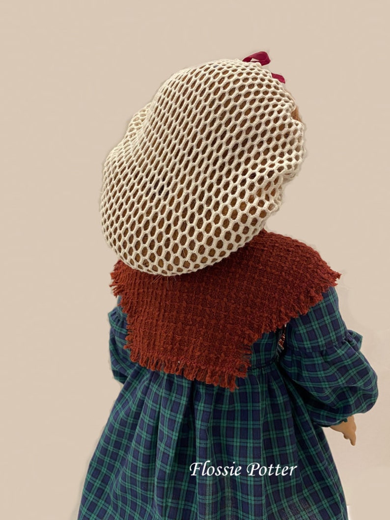 May include: A doll wearing a white mesh hairnet with a burgundy bow, a brown shawl, and a green and blue plaid dress. The doll's name, "Flossie Potter", is written on the dress.