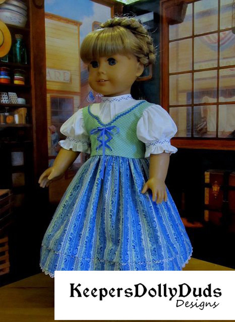 May include: A doll wearing a blue and green dress with a white blouse and a blue ribbon. The dress has a lace trim and a striped pattern. The doll is standing in front of a wooden shelf with various items on it.