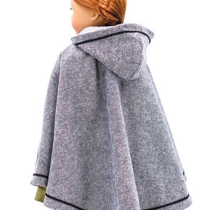 May include: A gray hooded cape with black trim for a doll. The cape is made of a soft, textured fabric. KeepersDollyDuds Designs is printed on the bottom of the cape.