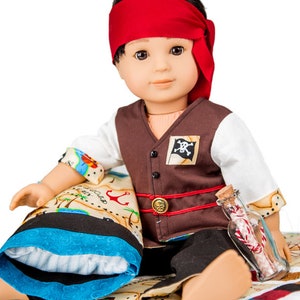 May include: A doll dressed as a pirate, wearing a brown vest with a skull and crossbones patch, a red bandana, and black pants. The doll is holding a glass bottle with a rolled-up piece of paper inside. The doll is sitting on a bed with a blue and white pillow and a map printed on the fabric.