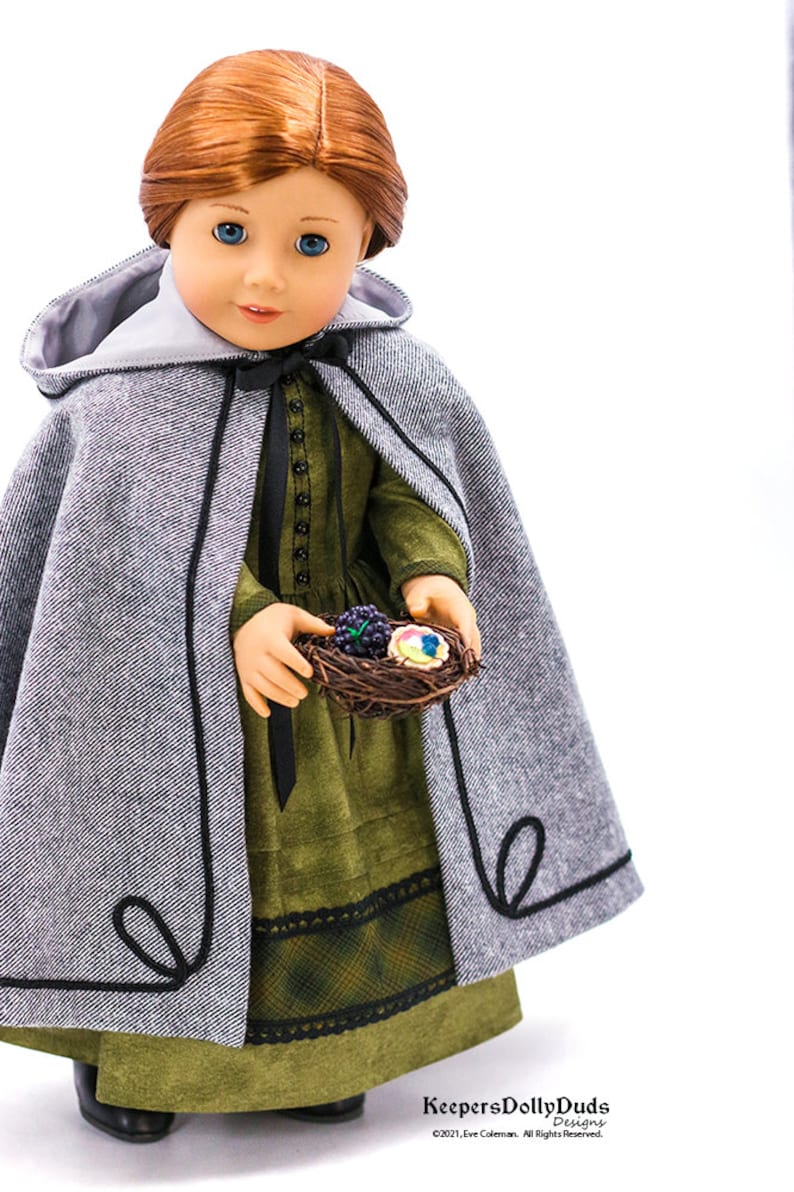 May include: A doll wearing a gray hooded cape with black trim, a green dress with a black lace trim, and black shoes. The doll is holding a small bird's nest with colorful eggs and berries. KeepersDollyDuds Designs &copy;2021 Eve Coleman. All Rights Reserved.