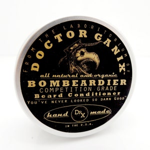 May include: A black and gold tin container with the text "From the Laboratorium of Doctor Gani X" and "All natural and organic Bombeardier Competition Grade Beard Conditioner. You've never looked so damn good." The tin also has the text "Hand made" and "Dr. X" in the center.