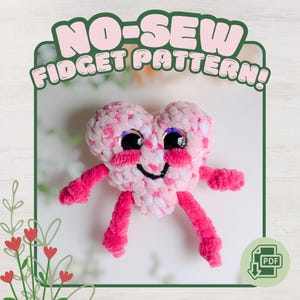 Op de afbeelding: Een pluche hartvormig speeltje met een gemêleerde roze en witte textuur, grote zwarte veiligheidsogen, een geborduurde zwarte glimlach en felroze chenille armen en benen. De tekst NO-SEW FIDGET PATTERN staat bovenaan met een PDF-icoon onderaan.