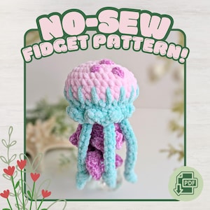 Könnte beinhalten: Ein handgefertigtes Quallen-Spielzeug aus Plüsch in Rosa, Blau und Lila. Die Qualle hat eine abgerundete Oberseite mit kleinen rosa Kreisen und langen, herabhängenden Tentakeln. Der Text "NO-SEW FIDGET PATTERN!" ist zu sehen.