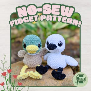 May include: Two crocheted plush toys, one a green and tan duck with yellow feet and the other a white swan with black feet, both featuring large dark eyes. The text NO-SEW FIDGET PATTERN! is displayed at the top, with a PDF icon in the corner.