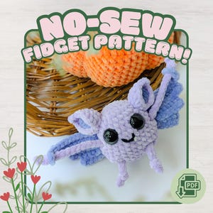 May include: A crochet bat toy made of light purple yarn with large black safety eyes and a small stitched mouth. The text NO-SEW FIDGET PATTERN is displayed at the top. A PDF icon is in the bottom right corner, and an orange pumpkin is visible.