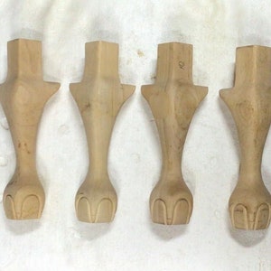 May include: Four unfinished wooden furniture legs with a carved design at the bottom. The legs are all the same size and shape.