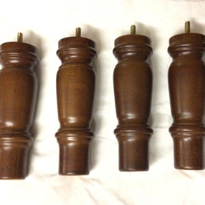 May include: Four brown wooden furniture legs with a slightly tapered design and a rounded top. The legs have a dark brown stain and a smooth finish.