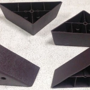 May include: Four brown plastic furniture legs in a triangular shape. The legs have a textured surface and are designed to be attached to furniture.
