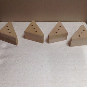 May include: Four wooden triangular blocks with holes drilled in them. The blocks are light brown in color and are arranged in a row on a white surface.