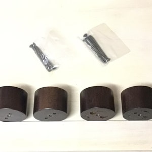 May include: Four dark brown wooden furniture legs with screw holes and four black screws in a plastic bag.