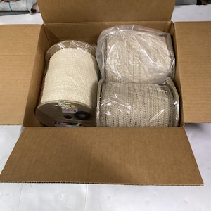 May include: A cardboard box filled with four spools of beige and off-white fabric trim. The spools are wrapped in clear plastic and labeled "ACE #16".
