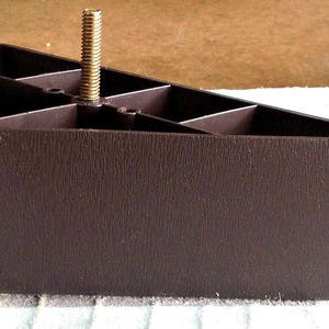 May include: A brown plastic furniture leg with a threaded metal screw. The leg is designed to raise the height of furniture.