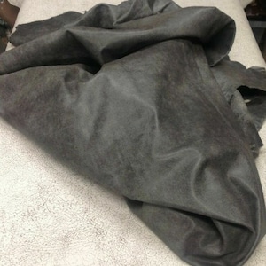 May include: A piece of dark gray suede fabric, folded and lying on a white textured surface.