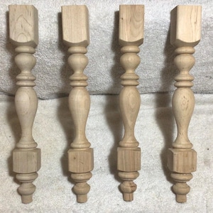May include: Four unfinished wooden table legs. Each leg has a square top, a turned central section with a bulbous shape, and a square base. The legs are made of light-colored wood and are ready for finishing.