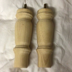 May include: Two unfinished wooden furniture legs with a turned design. The legs are approximately 5 inches tall and have a diameter of 2 inches.