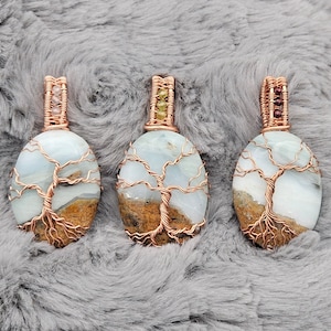 May include: Three wire-wrapped tree of life pendants with blue agate stones. Each pendant features a copper wire tree design and is accented with small gemstone beads.