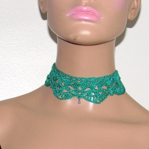 May include: A vibrant emerald green crochet choker necklace featuring an intricate scalloped lace pattern. The design includes a delicate, small, singular purple bead accent suspended from the center of the lower edge of the crocheted fabric.