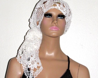 May include: White crocheted head scarf with a floral design. The scarf is tied in a knot at the back of the head and drapes down the back of the neck.