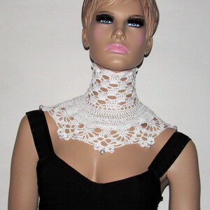 Puede incluir: Collar blanco de ganchillo con detalles de perlas. El collar es un dise&ntilde;o amplio y abierto con un borde festoneado.