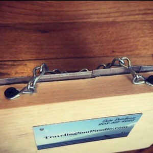 May include: A wooden box with two metal chains attached to the top. The box has a business card attached to the bottom with the text "TravelingSoulStudio.com".