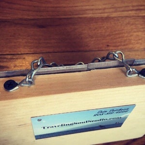 May include: A wooden box with two metal chains attached to the top. The box is closed and has a business card attached to the front that reads "Traveling Soul Studios".