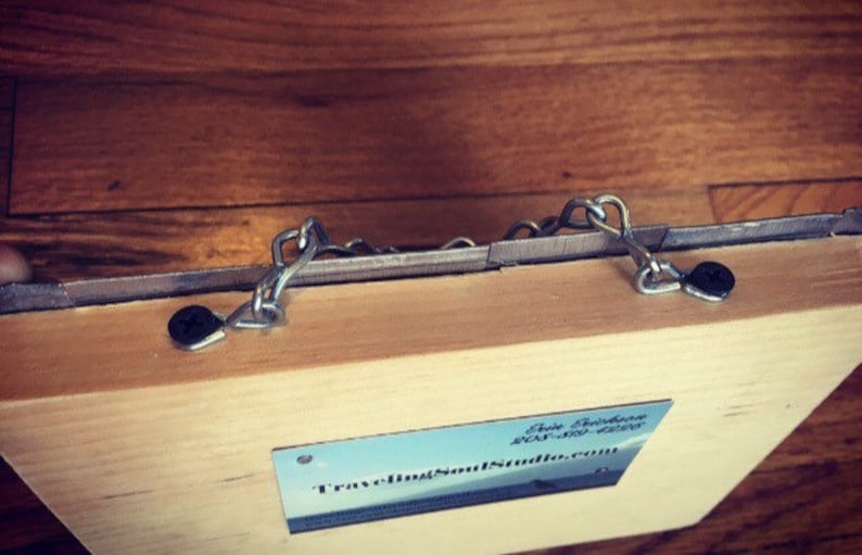 May include: A wooden box with two metal chains attached to the top. The box is closed and has a business card attached to the front that reads "Traveling Soul Studios".