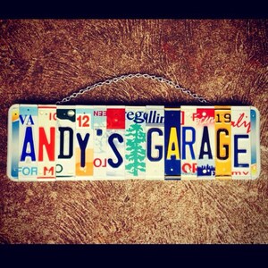 Może przedstawiać: Kolorowy znak wykonany z tablic rejestracyjnych z napisem "ANDY'S GARAGE". Znak jest zawieszony na łańcuchu.