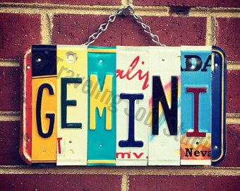 May include: A colorful sign spelling out the word "GEMINI" using repurposed license plates. The letters are in black and the plates are in various colors, including yellow, blue, red, and white.