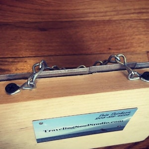Puede incluir: Una caja de madera con un cierre de metal y una tarjeta de visita que dice "Traveling Soul Studio.com".