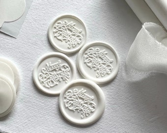 Puede incluir: Cuatro sellos de cera blanca con las palabras "Merry Christmas" grabadas en una escritura decorativa.