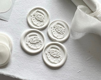 May include: Four white wax seals with a raised image of Santa Claus's face. The seals are on a white surface.