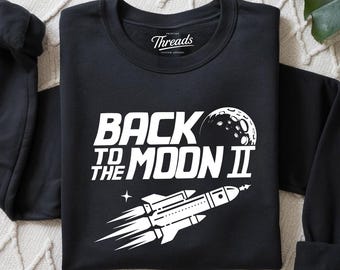 Koszulka „Powrót na Księżyc” | Grafika z rakietą retro | Koszulka z epoki kosmicznej | Minimalistyczny styl vintage | Koszulka unisex