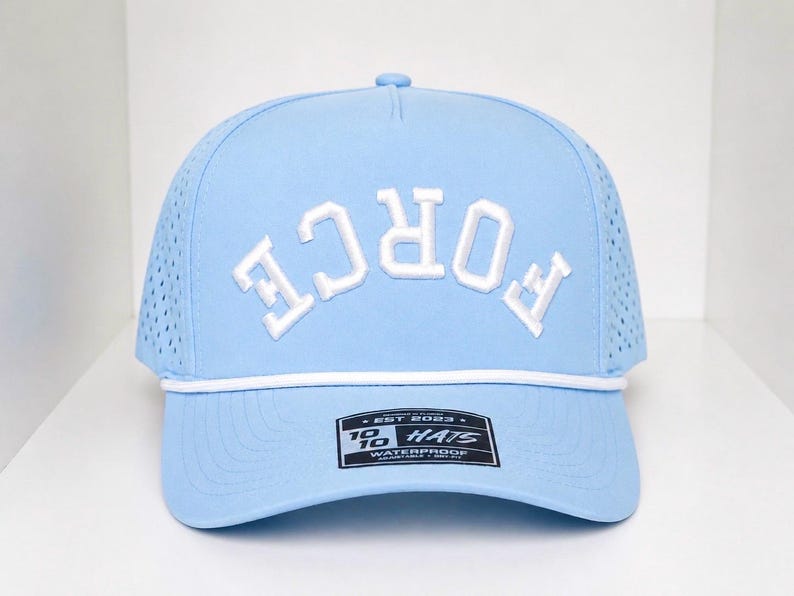 K&ouml;nnte beinhalten: Hellblaue Baseballkappe mit dem Wort "FORCE" in Wei&szlig;, das sich &uuml;ber die Vorderseite w&ouml;lbt. Die Kappe hat ein wei&szlig;es Seildetail und ein kleines rechteckiges Etikett. Die Kappe ist wasserdicht.
