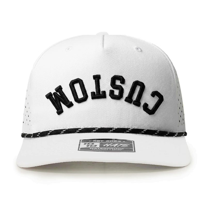 K&ouml;nnte beinhalten: Wei&szlig;e Baseballkappe mit dem Wort "CUSTOM" in Schwarz auf der Vorderseite gestickt. Sie hat eine schwarz-wei&szlig;e Seildetail am Rand und ein kleines Etikett. Die Kappe hat kleine Bel&uuml;ftungsl&ouml;cher.
