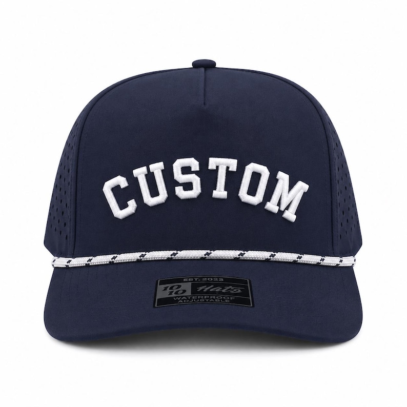 Puede incluir: Gorra de b&eacute;isbol azul marino con la palabra "CUSTOM" en blanco, arqueada en la parte delantera. La gorra tiene un detalle de cuerda blanca y negra a lo largo del borde y una peque&ntilde;a etiqueta que dice "10/10 Hats".
