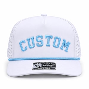 Puede incluir: Gorra de b&eacute;isbol blanca con la palabra "CUSTOM" bordada en azul claro. La gorra tiene un dise&ntilde;o de malla perforada en los laterales y un detalle de cuerda azul claro. La etiqueta dice "10/10 Hats, Waterproof, Adjustable."