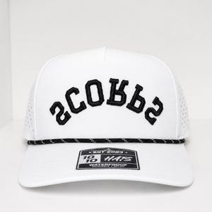 K&ouml;nnte beinhalten: Wei&szlig;e Baseballkappe mit dem Wort "SCOBBS" in Schwarz auf der Vorderseite gestickt. Die Kappe hat ein schwarz-wei&szlig;es Seildetail am Rand und ein kleines Etikett auf der Vorderseite. Der Hut ist wasserdicht.