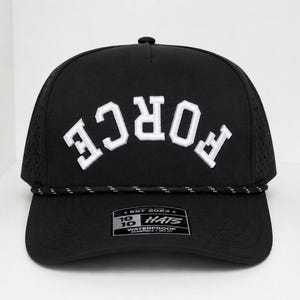 K&ouml;nnte beinhalten: Schwarze Baseballkappe mit dem wei&szlig;en Wort "FORCE" in einem Bogen &uuml;ber der Vorderseite. Die Kappe hat einen gebogenen Schirm, ein schwarz-wei&szlig;es Seildetail und ein kleines Etikett auf der Vorderseite. Die Kappe ist wasserdicht.