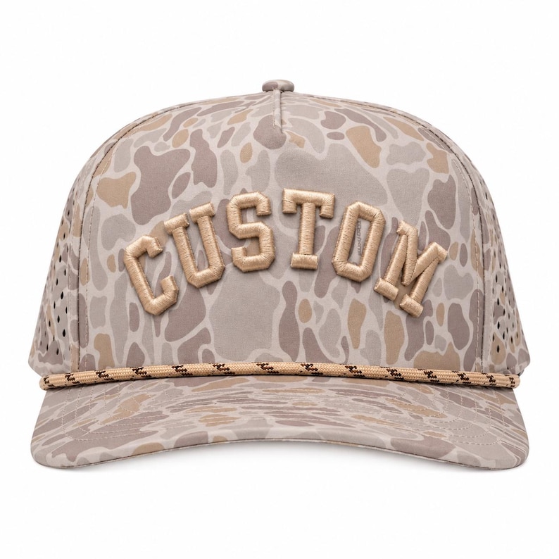 Puede incluir: Gorra de b&eacute;isbol de camuflaje beige con la palabra "CUSTOM" bordada en beige claro. La gorra tiene un detalle de cuerda en el borde y paneles laterales de malla. Un accesorio elegante.