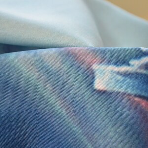 May include: Close-up of a blue fabric with a tie-dye pattern. The fabric has a subtle shimmer and a soft, textured feel.