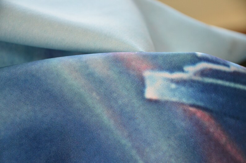 May include: Close-up of a blue fabric with a tie-dye pattern. The fabric has a subtle shimmer and a soft, textured feel.